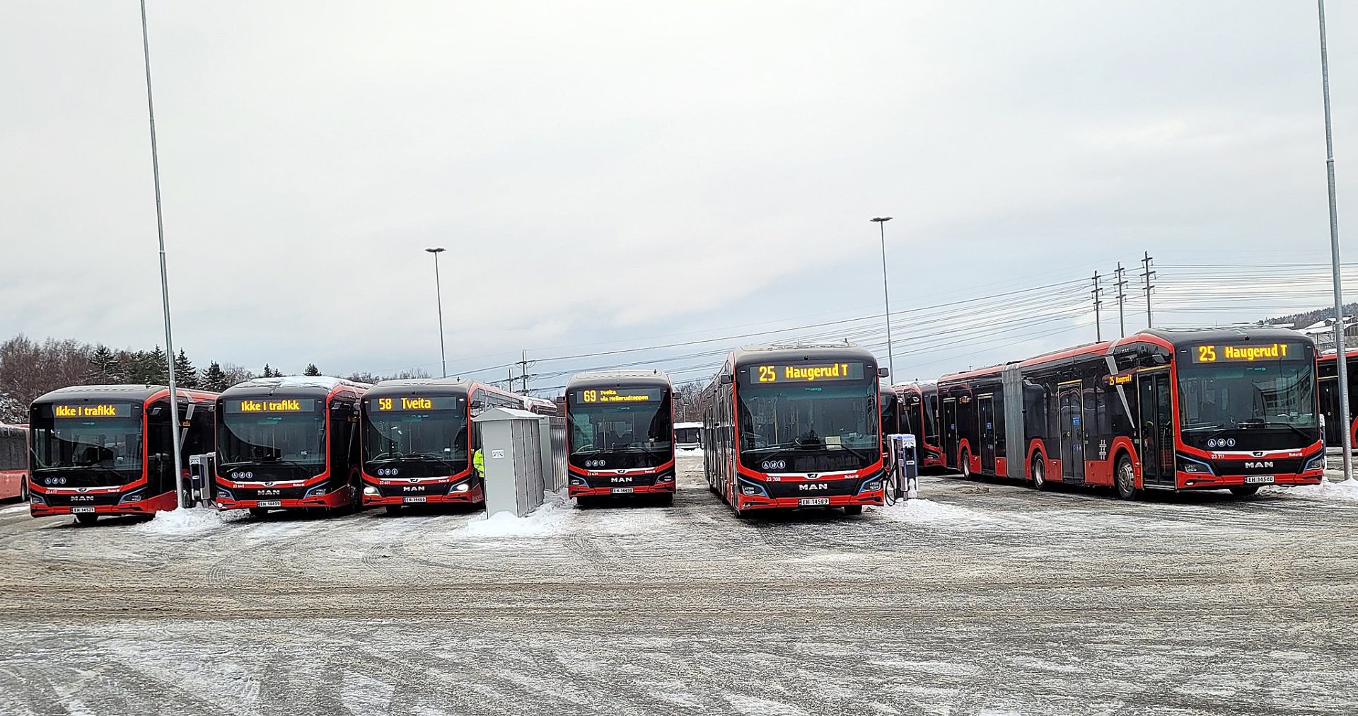 En rekke røde og hvite bybusser på en snødekt tomt, som viser forskjellige rutenumre og destinasjoner.