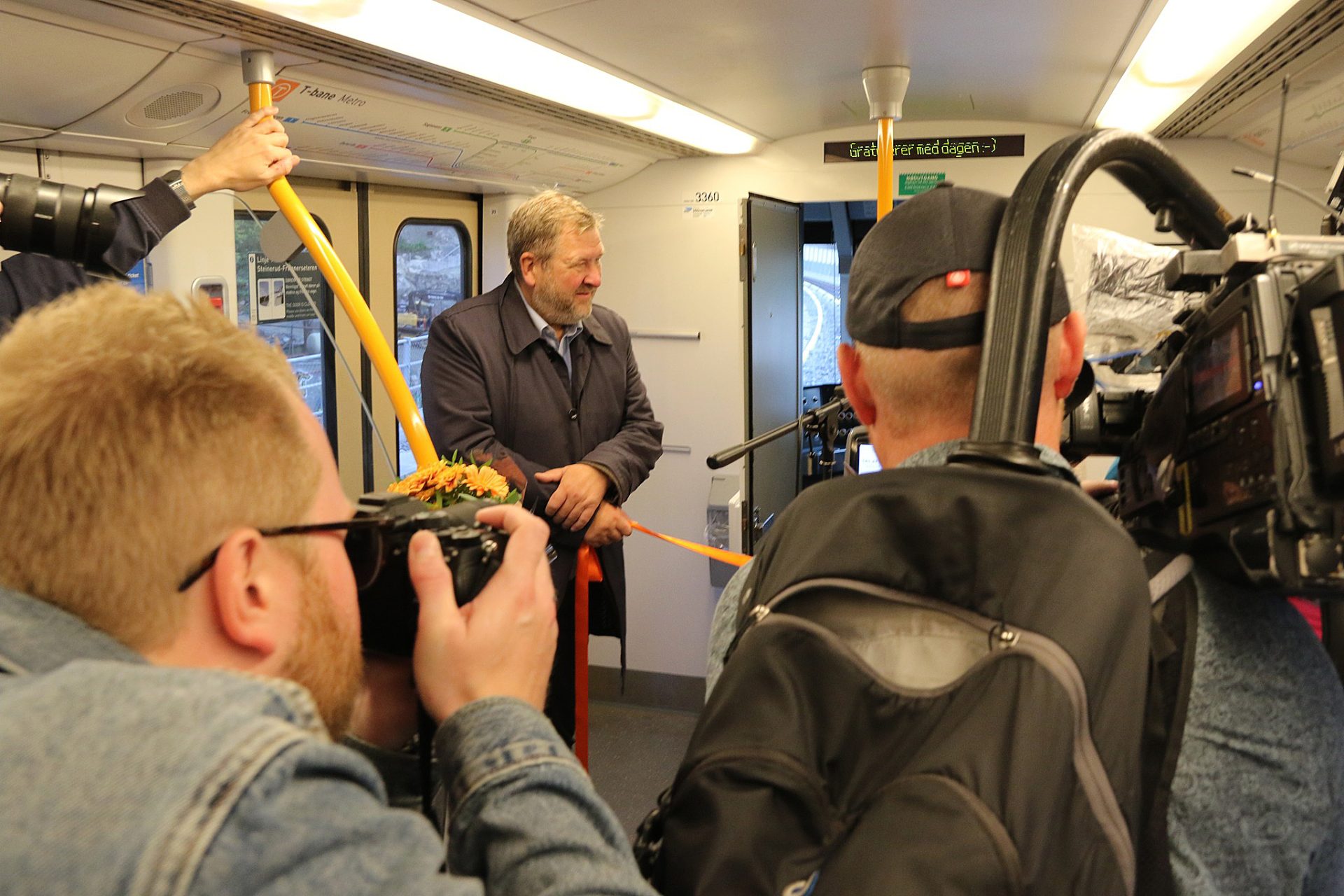 Ruters administrerende direktør, Bernt Reitan Jenssen, inne i en T-banevogn, klar til å klippe et bånd, mens han blir filmet og fotografert.