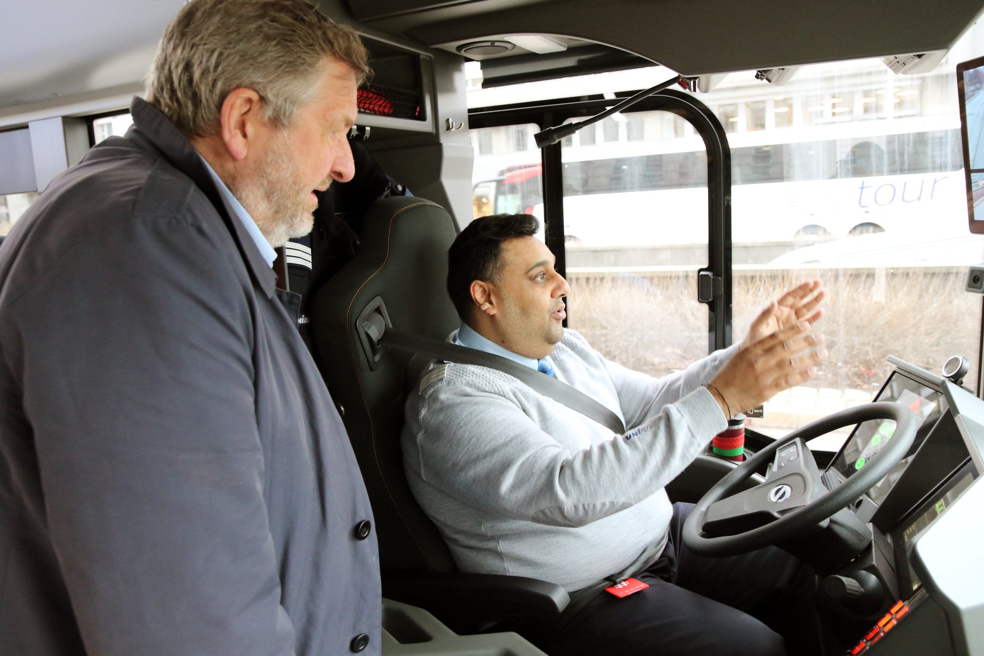  Ruter's CEO stands next to him and listens attentively to a driver who sits in the driver's seat of a bus and talks and gestures.